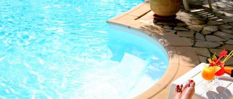 Un espace aménagé au bord de la piscine, avec un fauteuil de relaxation, un pot de fleurs et une table sur laquelle se trouvent une boisson et un arrangement floral.