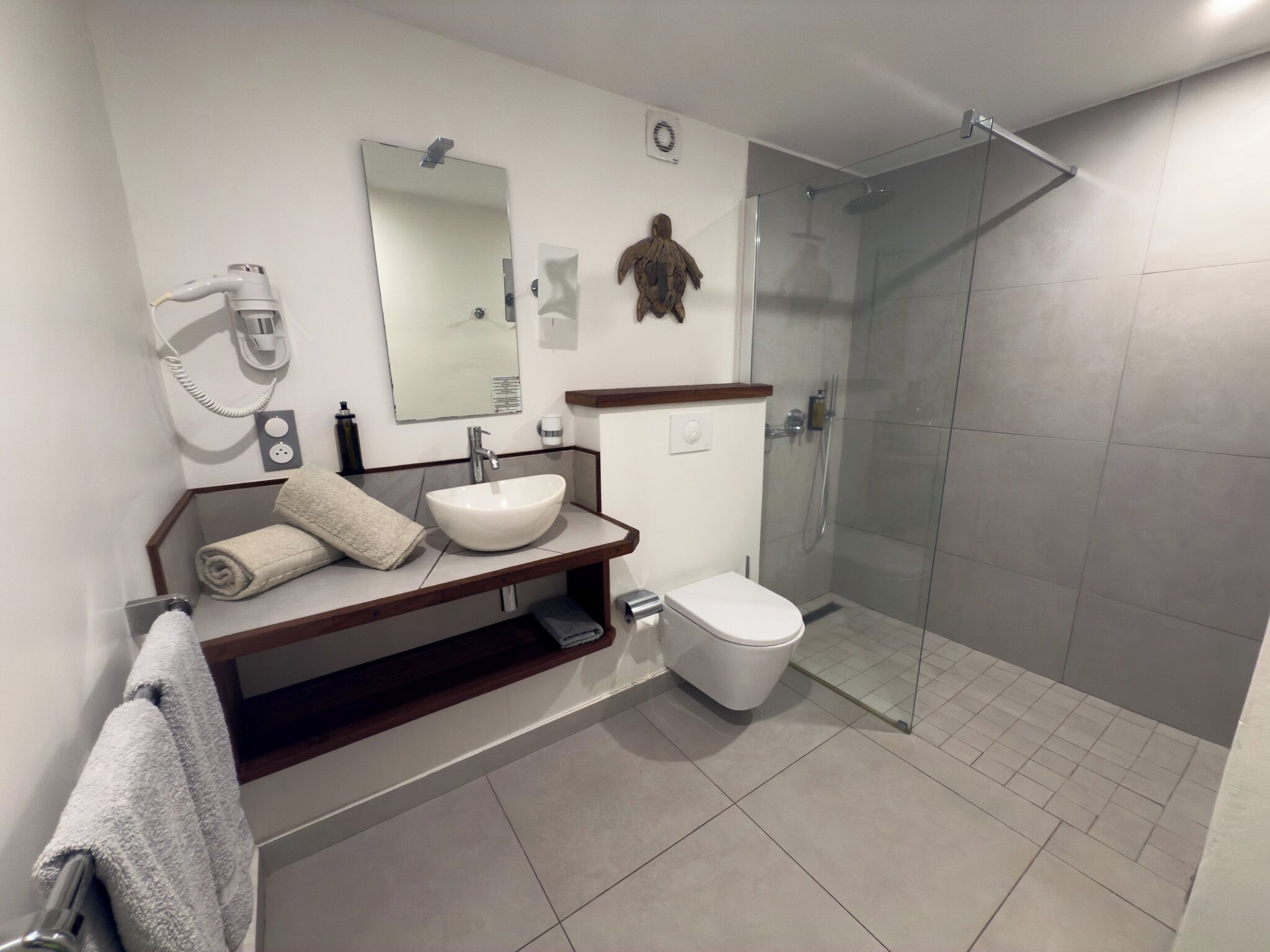 A modern bathroom with a glass shower enclosure, a white sink, and a towel rack.