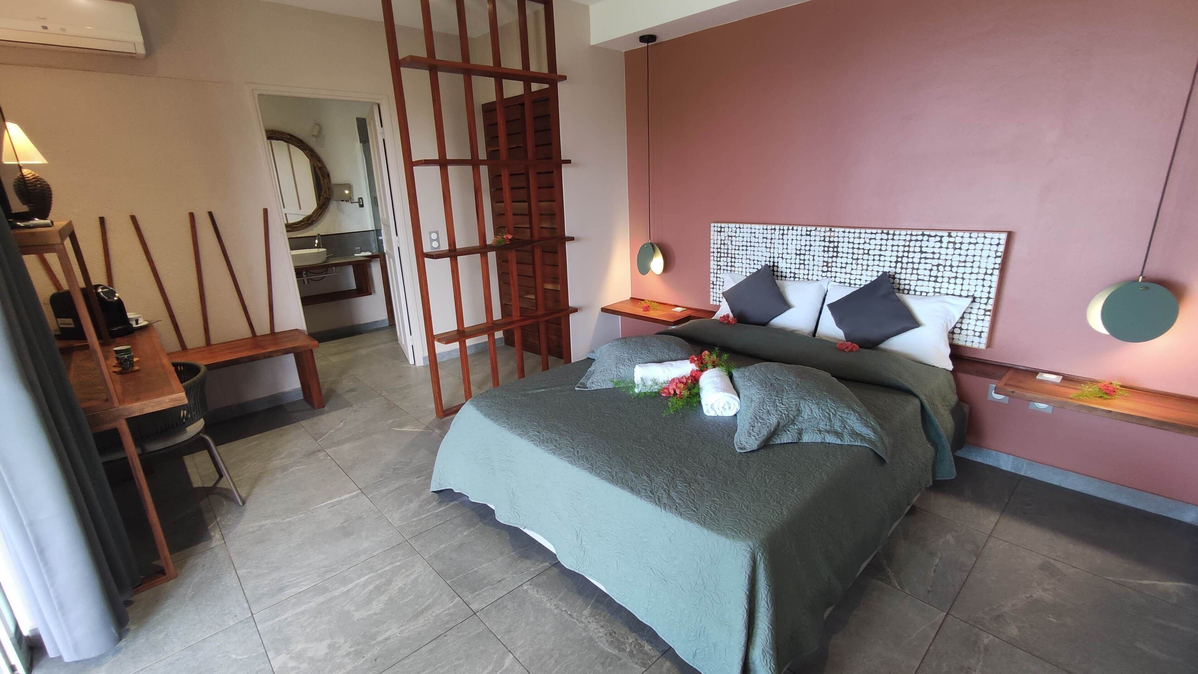 A bedroom with a bed, a desk, a chair, a mirror, and a wooden partition.