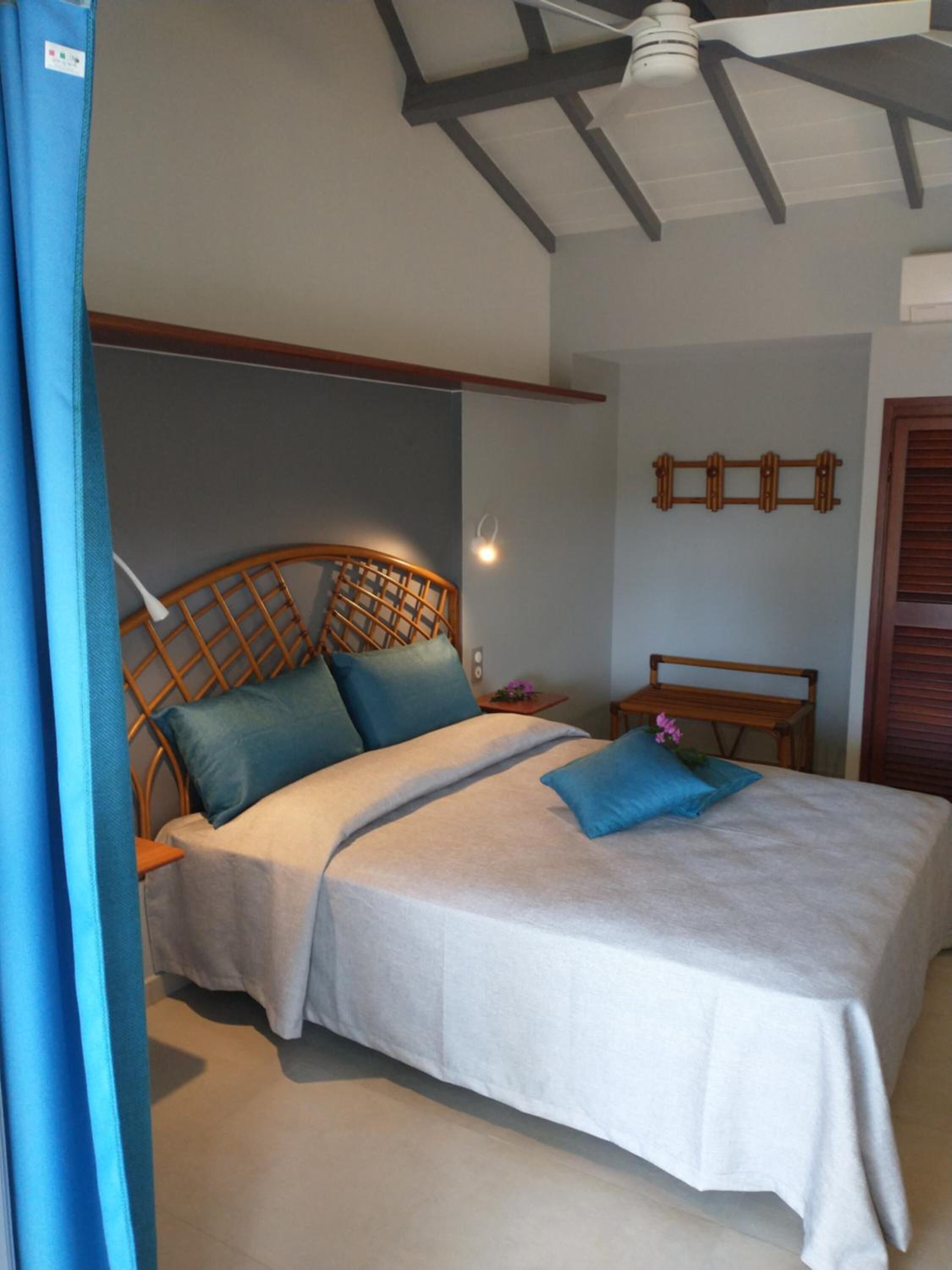 A bedroom with a bed, a wooden headboard, a nightstand, a wall-mounted light, and a ceiling fan.