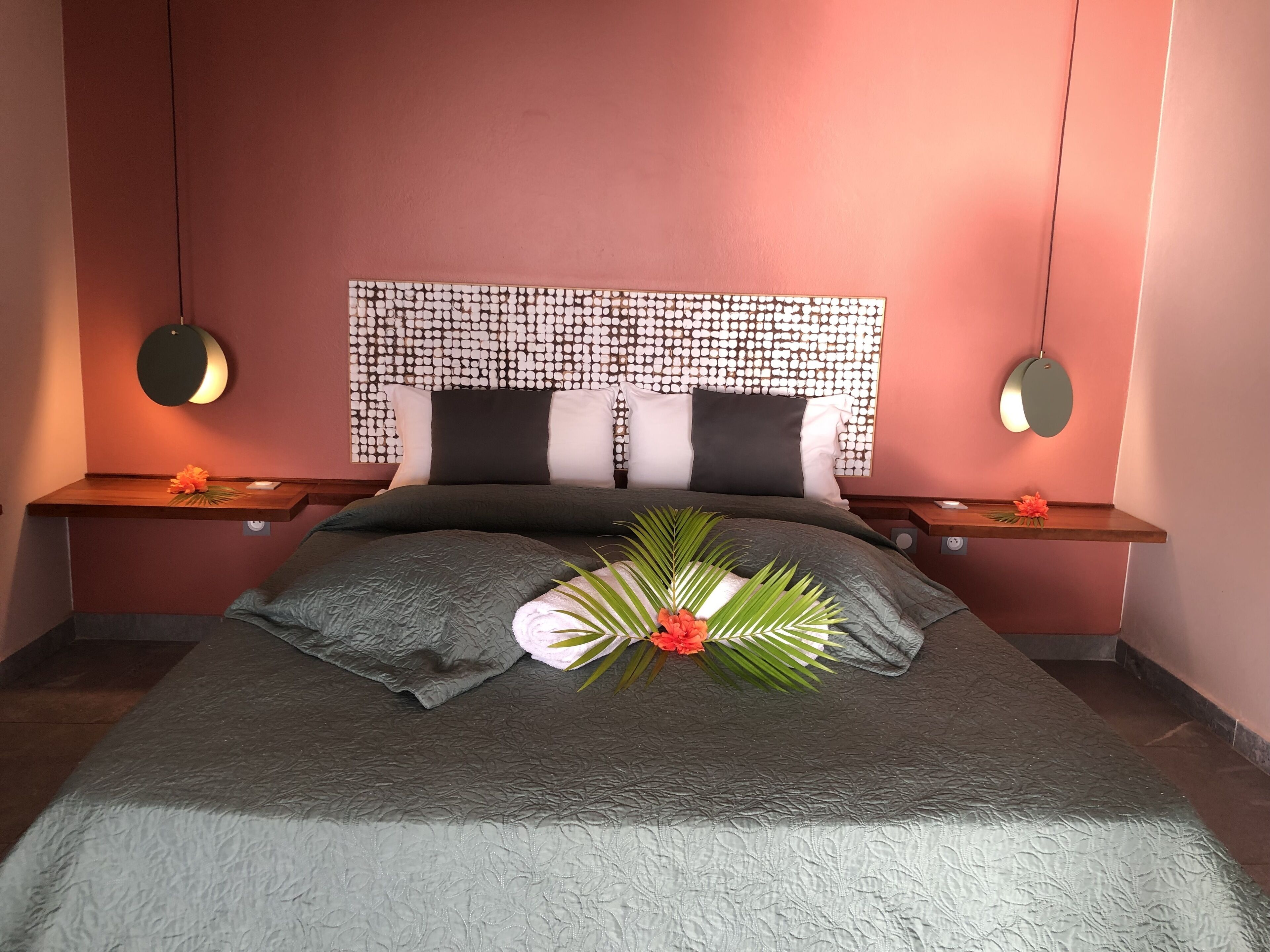 A neatly made bed with a patterned headboard, two bedside tables with lamps, and a decorative plant arrangement.