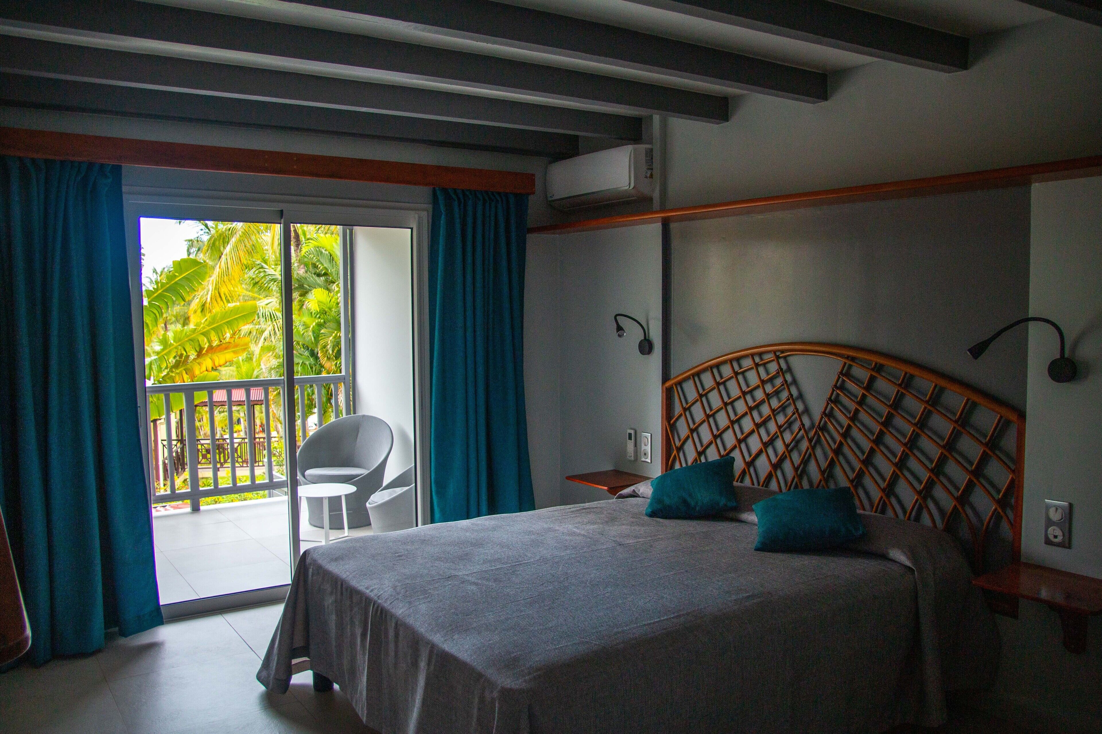 A bedroom with a bed, a chair, a small table, and a balcony with curtains.