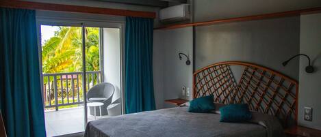 A bedroom with a bed, a chair, a small table, and a balcony with curtains.