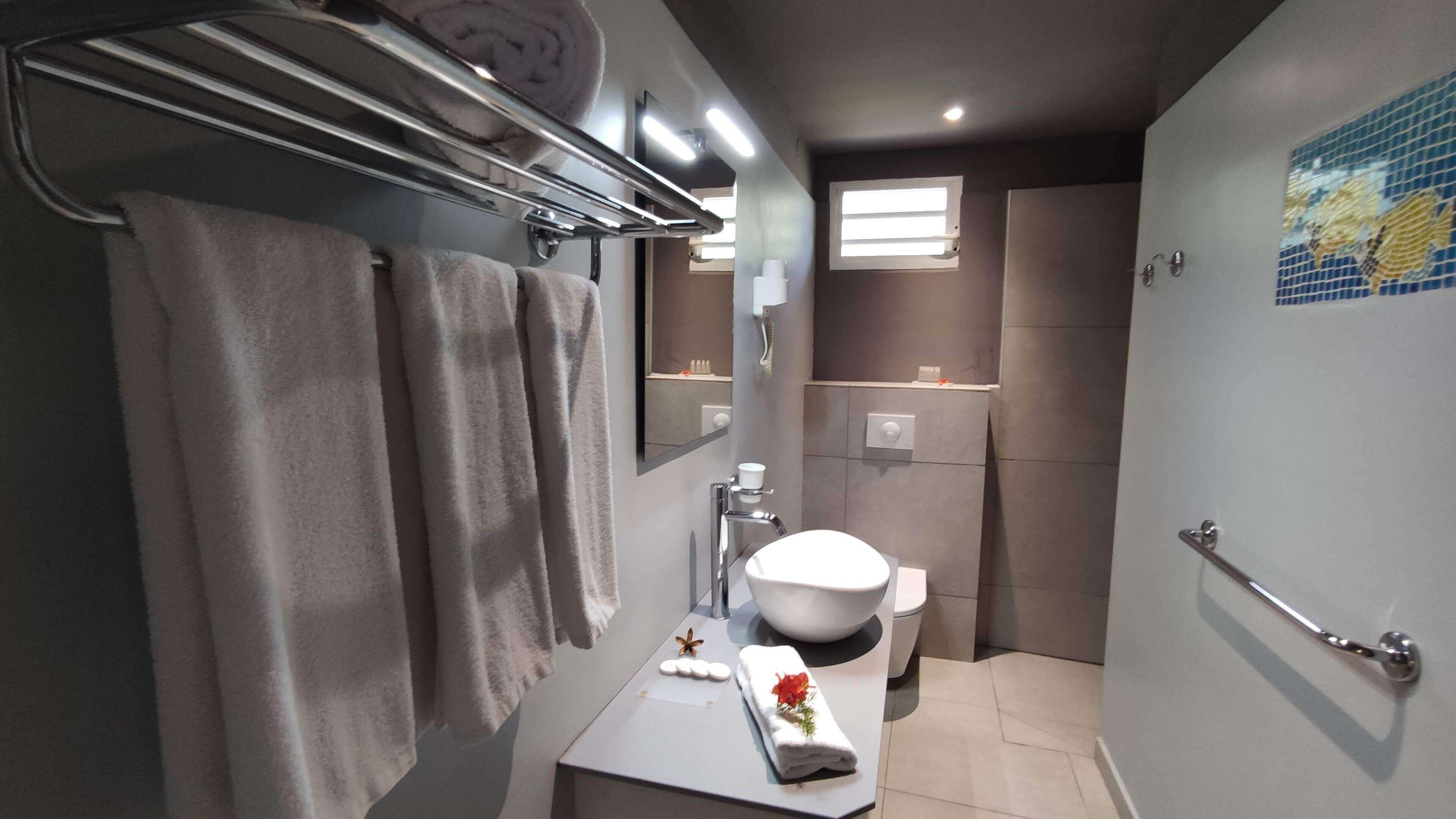 A modern bathroom with a white sink, mirror, and towel rack. There is a shower area with a glass door and a small window.