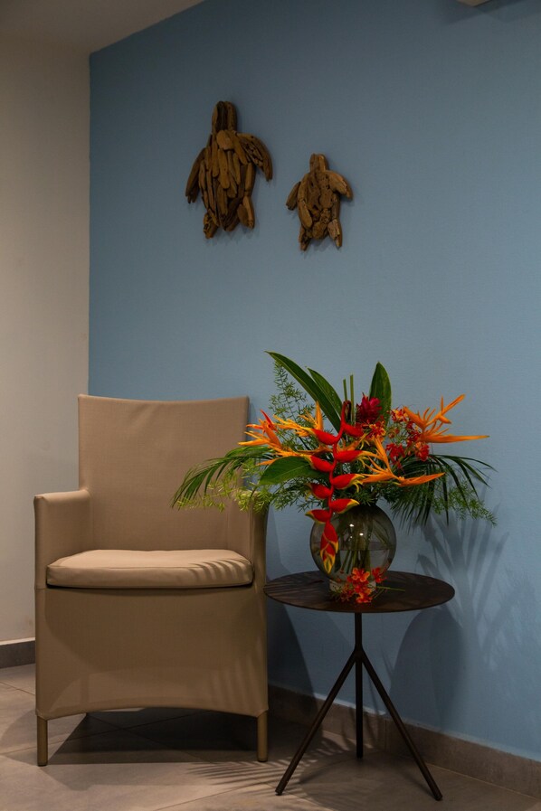 Un sillón color beige y una mesita redonda con un arreglo floral frente a una pared azul.