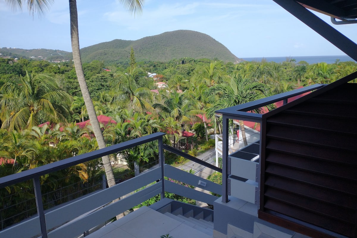 A balcony with a view of a lush landscape, including palm trees and a distant mountain.