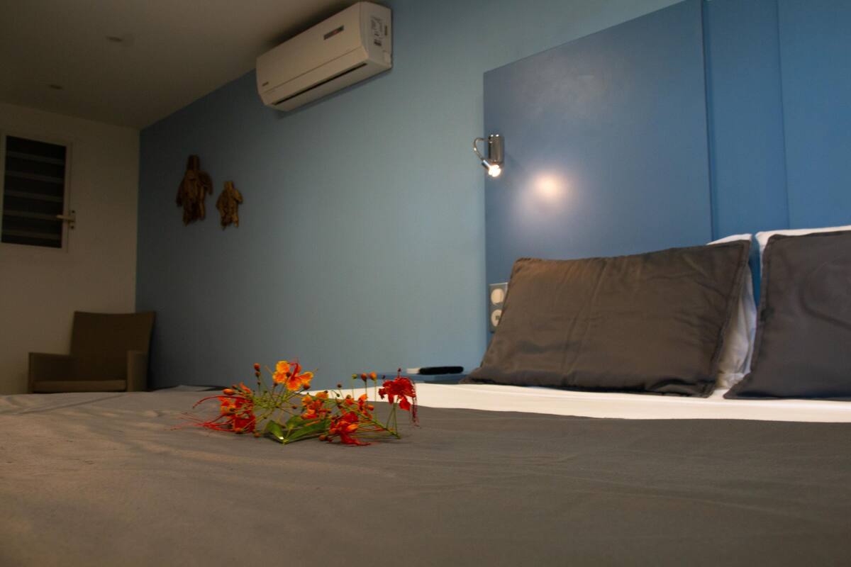 A bedroom with a bed, a nightstand, a wall-mounted air conditioner, and a wall-mounted lamp.