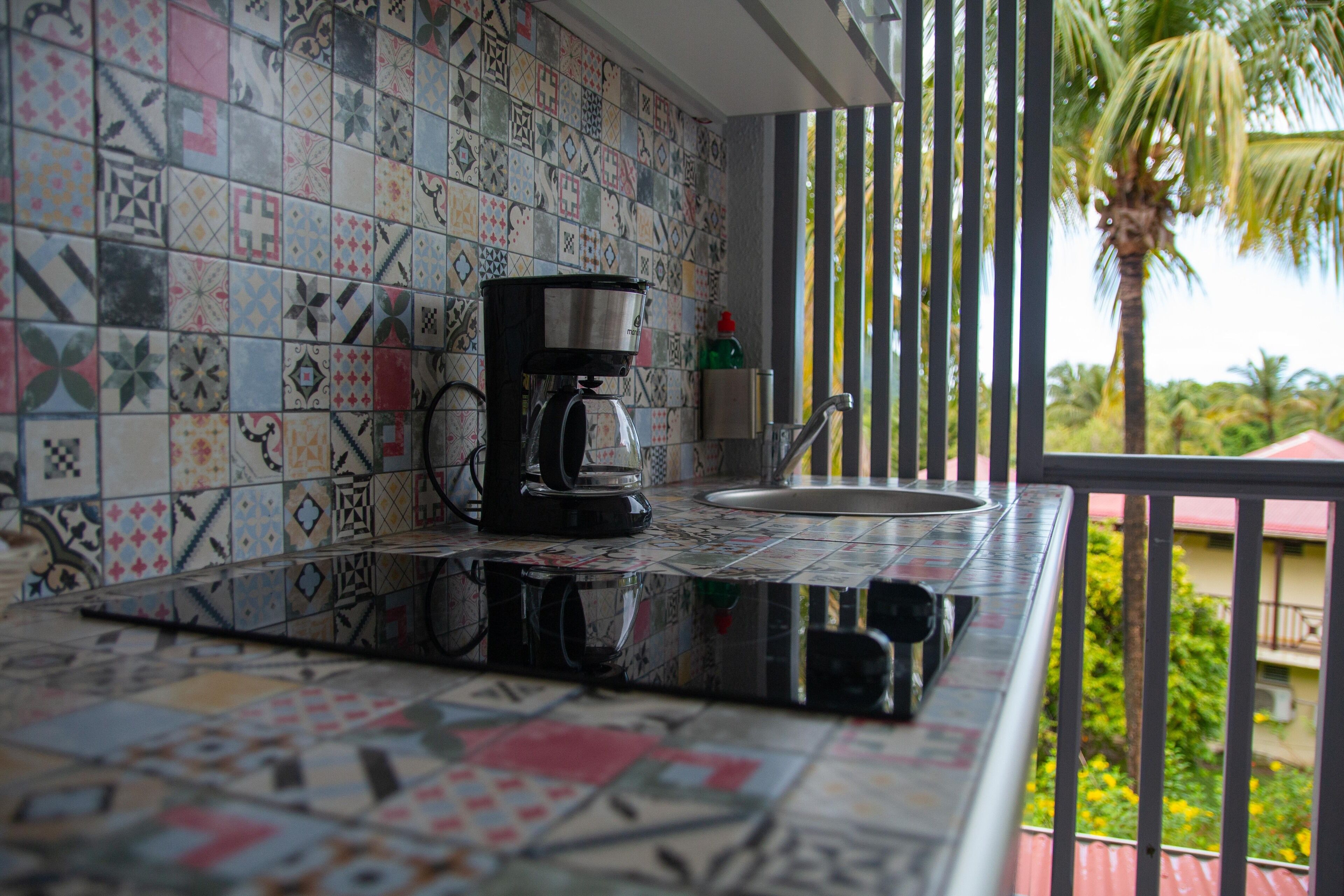 A kitchen with a coffee maker on the counter, a sink, and a patterned backsplash.