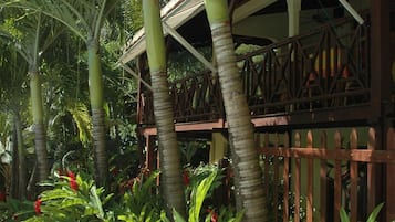 Un jardín tropical con palmeras, una terraza de madera y flores rojas.