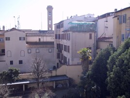 Un edificio de varios pisos con una torre del reloj, balcones y un espacio exterior cubierto.
