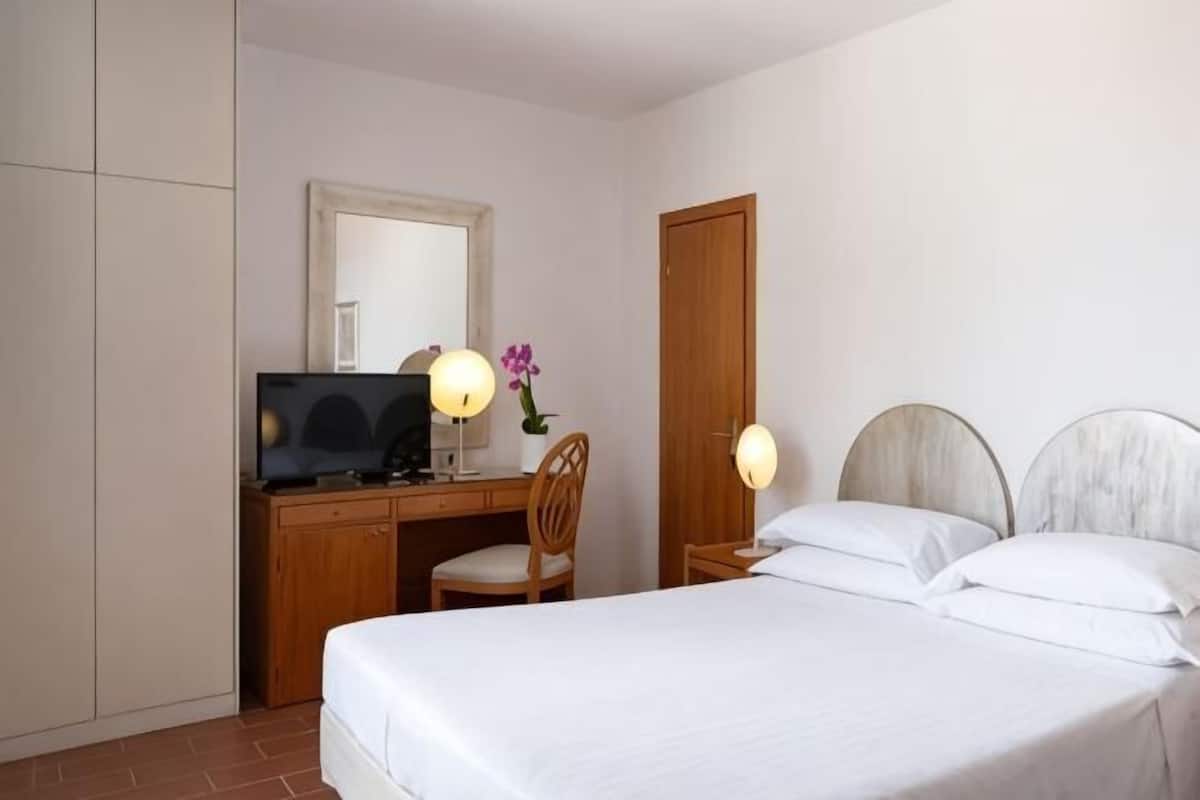 Ein Schlafzimmer mit einem Bett, einem Schreibtisch, einem Stuhl, einem Fernseher und einer Tür.