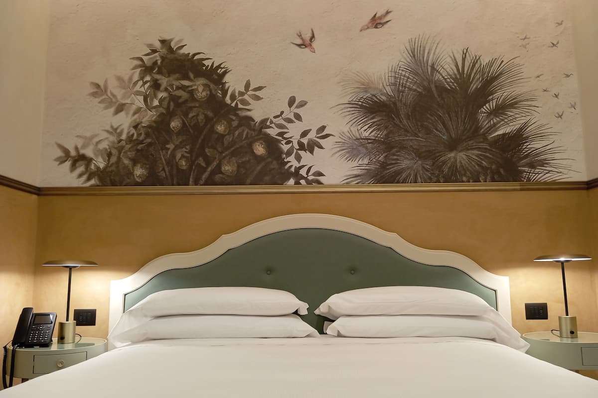 Ein Hotelzimmer mit einem großen Bett, zwei Nachttischen, einem Wandgemälde und einem Deckenventilator.