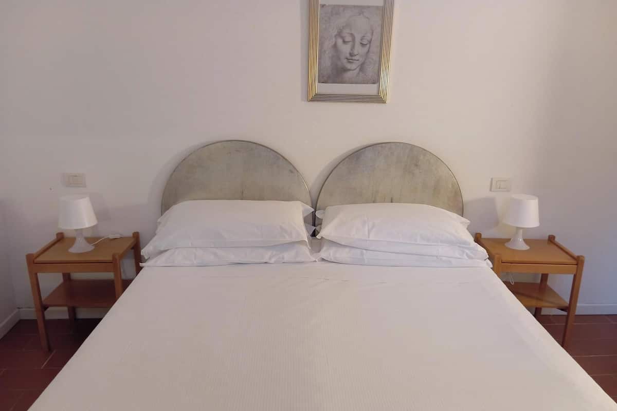 Ein ordentlich bezogenes Bett mit zwei Kissen und zwei Nachttischen, jeweils mit einer Lampe.