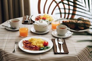 Une table de petit-déjeuner avec des assiettes d’œufs, de bacon et de pain grillé, des tasses de café et de thé, et une théière.