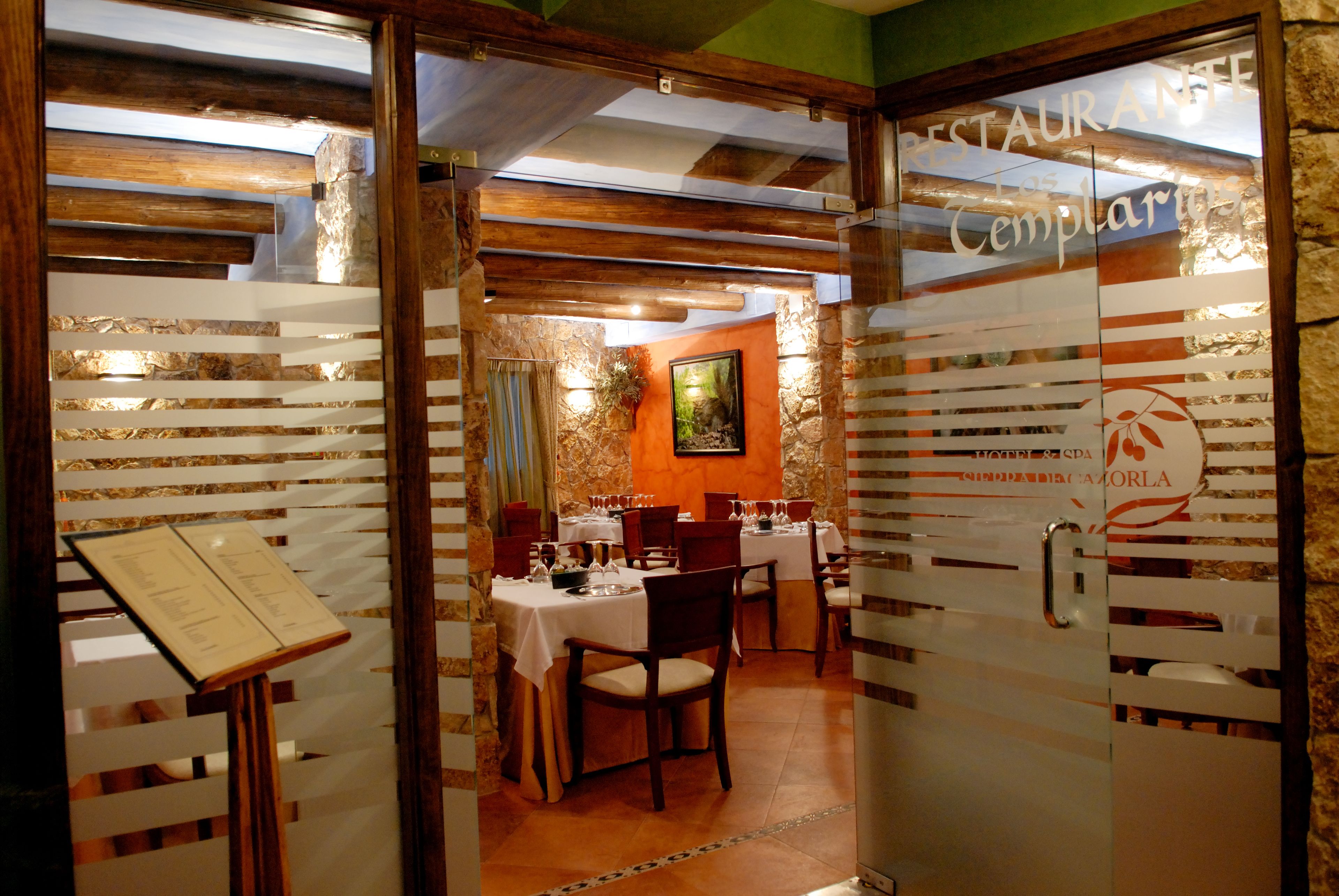 Interior de un restaurante con vigas de madera, paredes de piedra y un atril para el menú.
