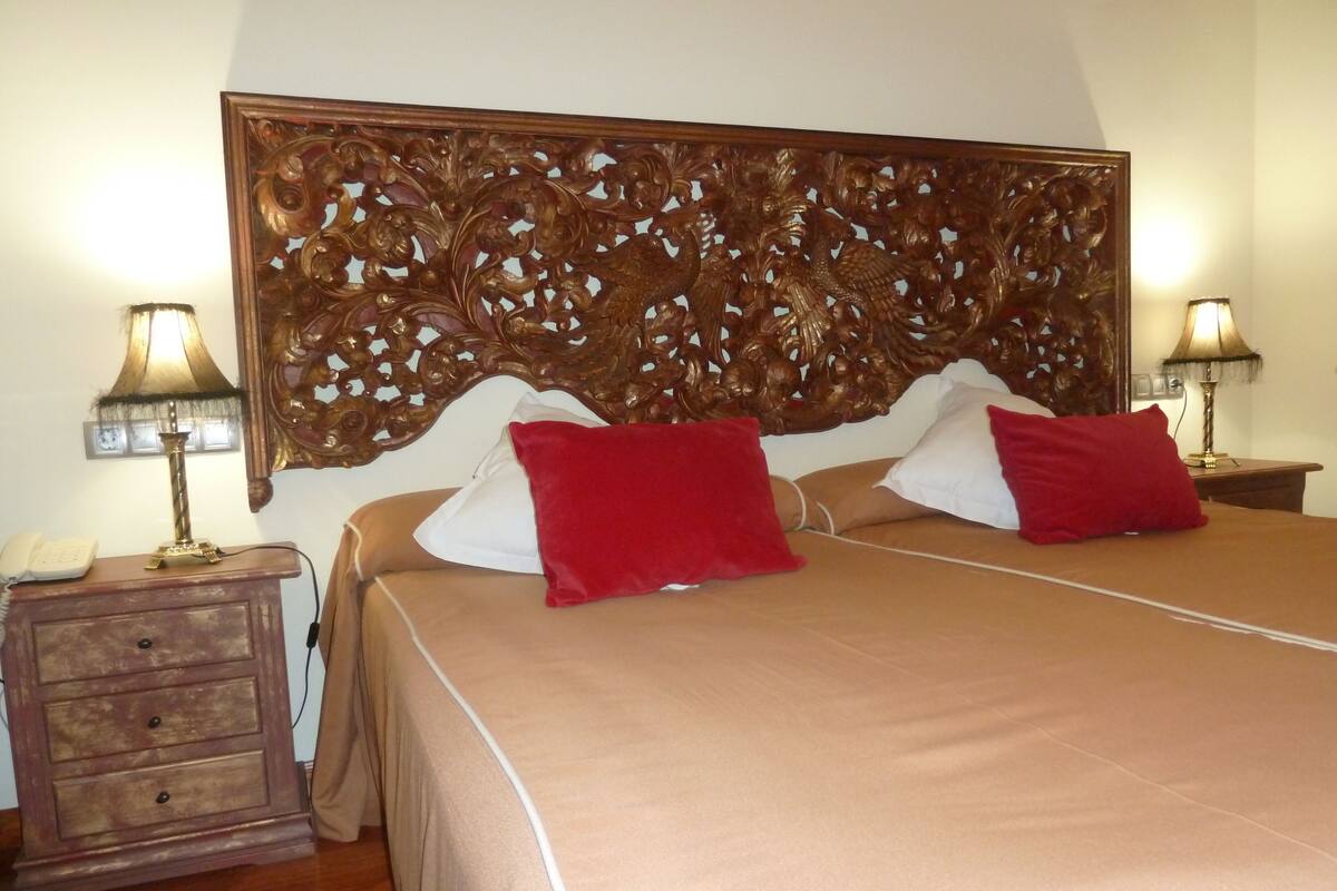 Una habitación de hotel con una cama grande, dos lámparas de noche, una mesita de noche de madera con teléfono y un cabecero decorativo.