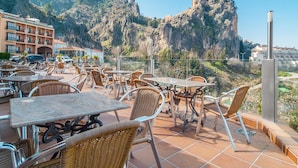 Une terrasse extérieure dotée de chaises et de tables en osier, offrant une vue sur un paysage montagneux.