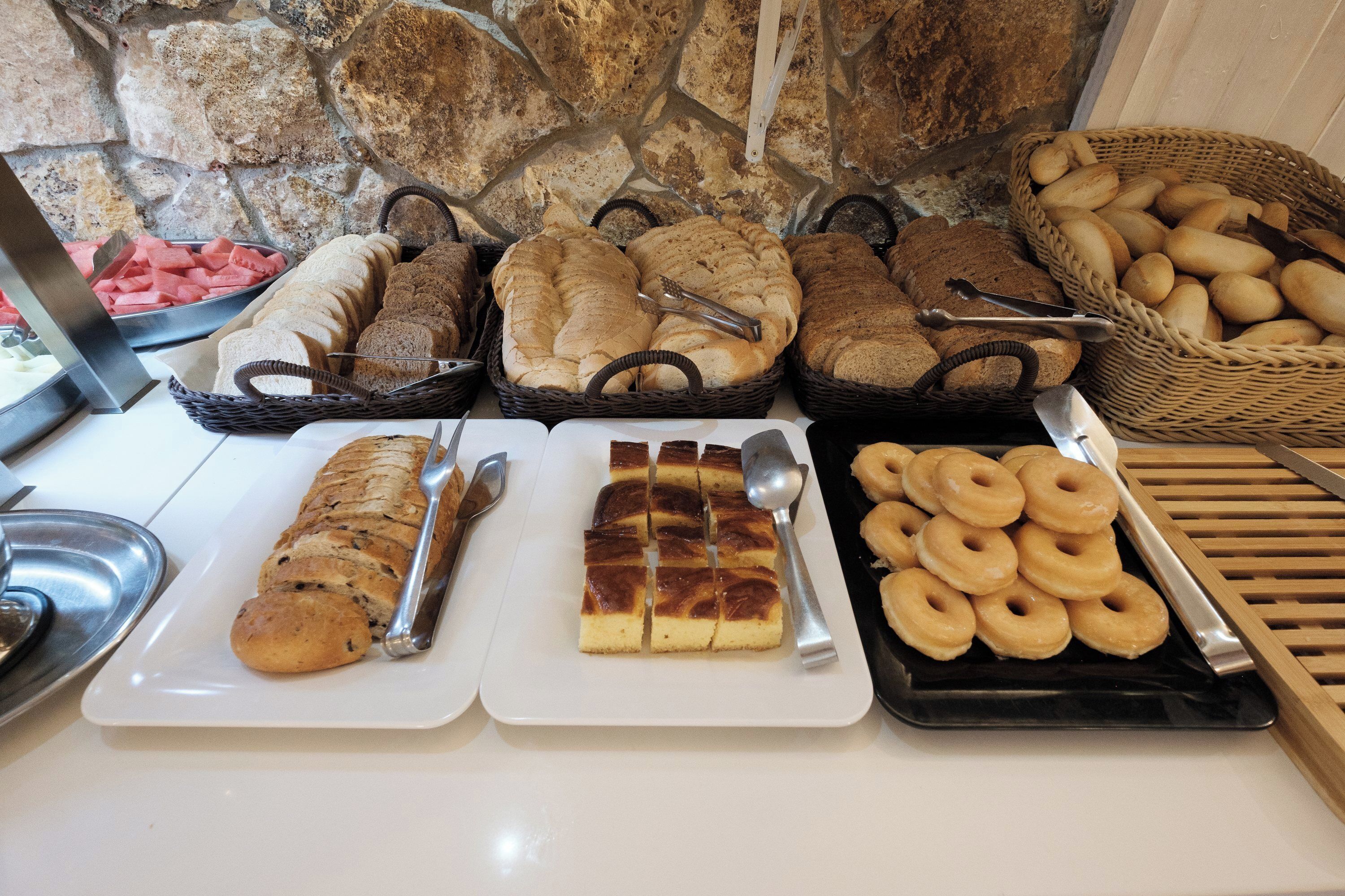 A breakfast buffet with various breads, pastries, and donuts.