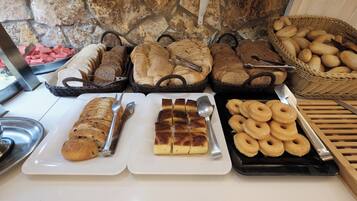 A breakfast buffet with various breads, pastries, and donuts.