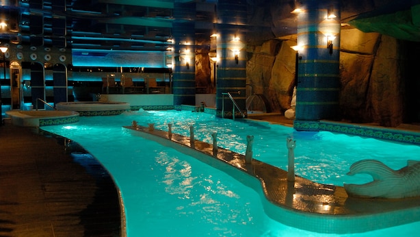 Une piscine intérieure dotée d’un îlot central, de murs en pierre et de nombreux luminaires.