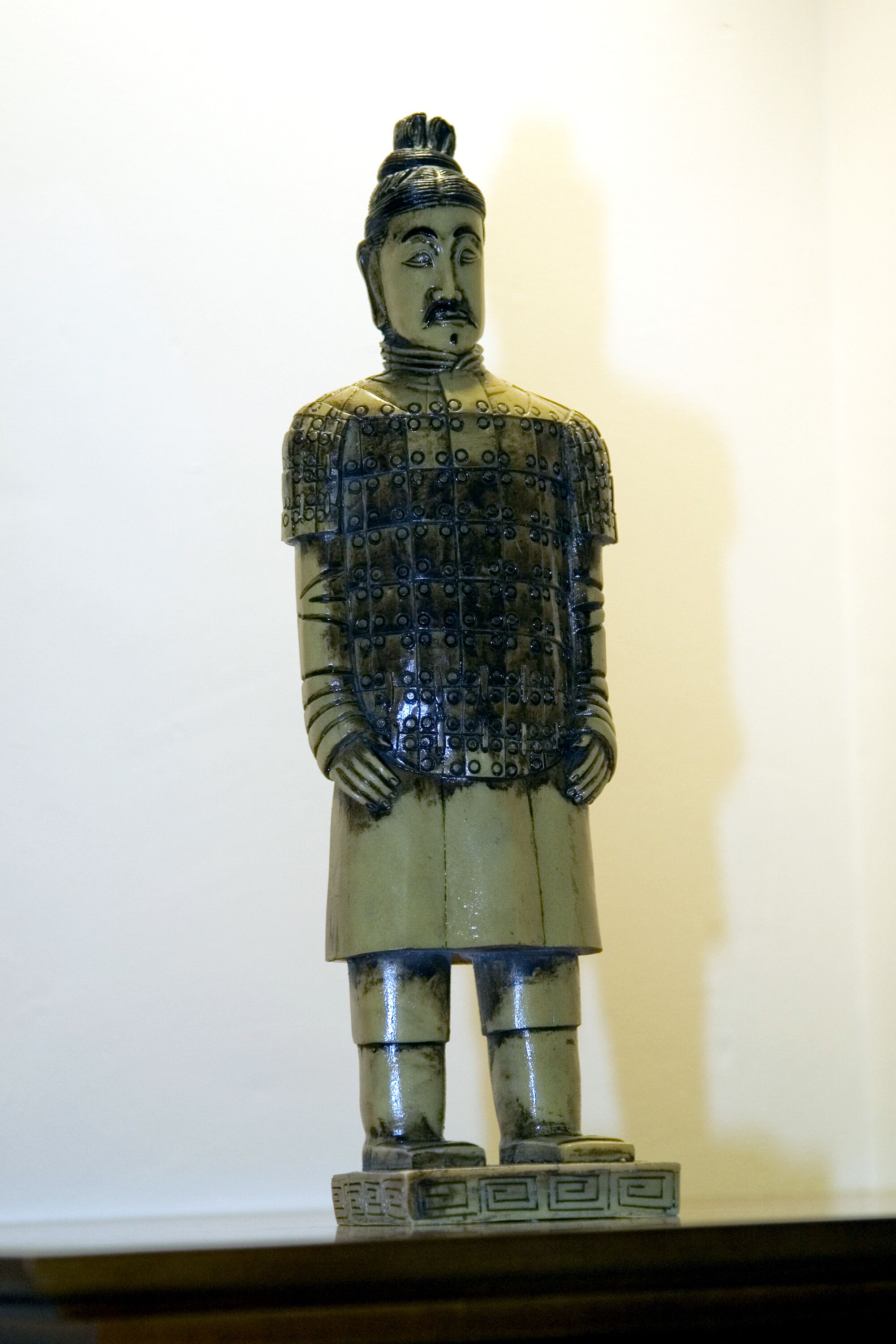 A statue of a figure in traditional attire, standing on a base with a geometric pattern.