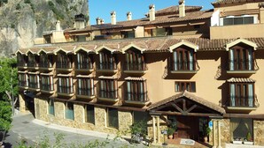 Un hôtel à la façade en pierre, doté de nombreux balcons et offrant une vue sur un château historique en arrière-plan.