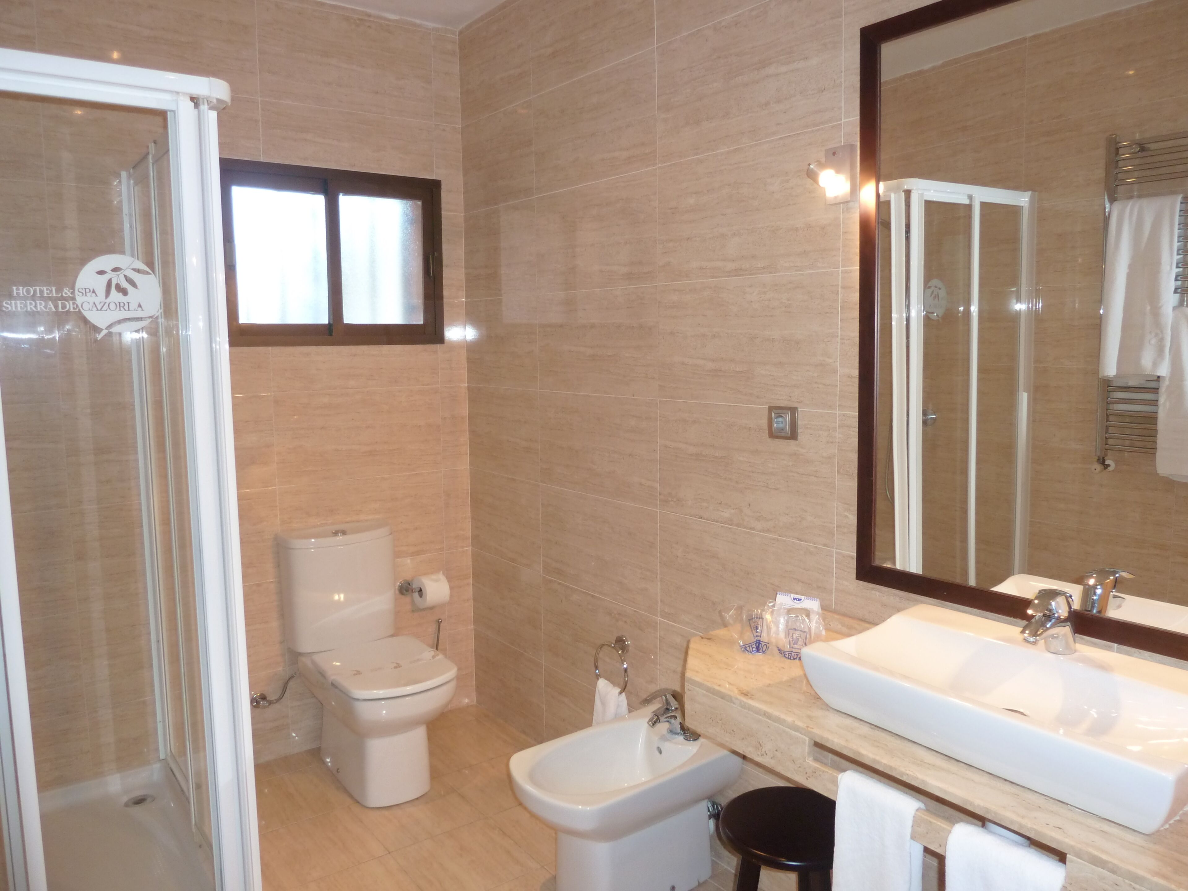 Een moderne badkamer met een douchecabine van glas, een toilet, een bidet en een grote wastafel met een spiegel erboven.