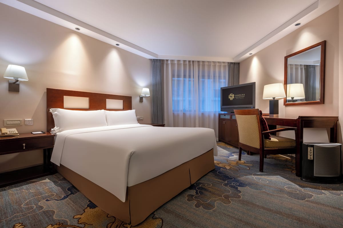 Une chambre d’hôtel avec un grand lit, un bureau avec une chaise, une télévision et un miroir.