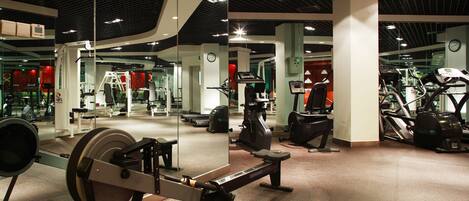 Un gimnasio con diversos equipos de ejercicio, incluyendo cintas de correr y máquinas de pesas, y un espejo grande que refleja el espacio.