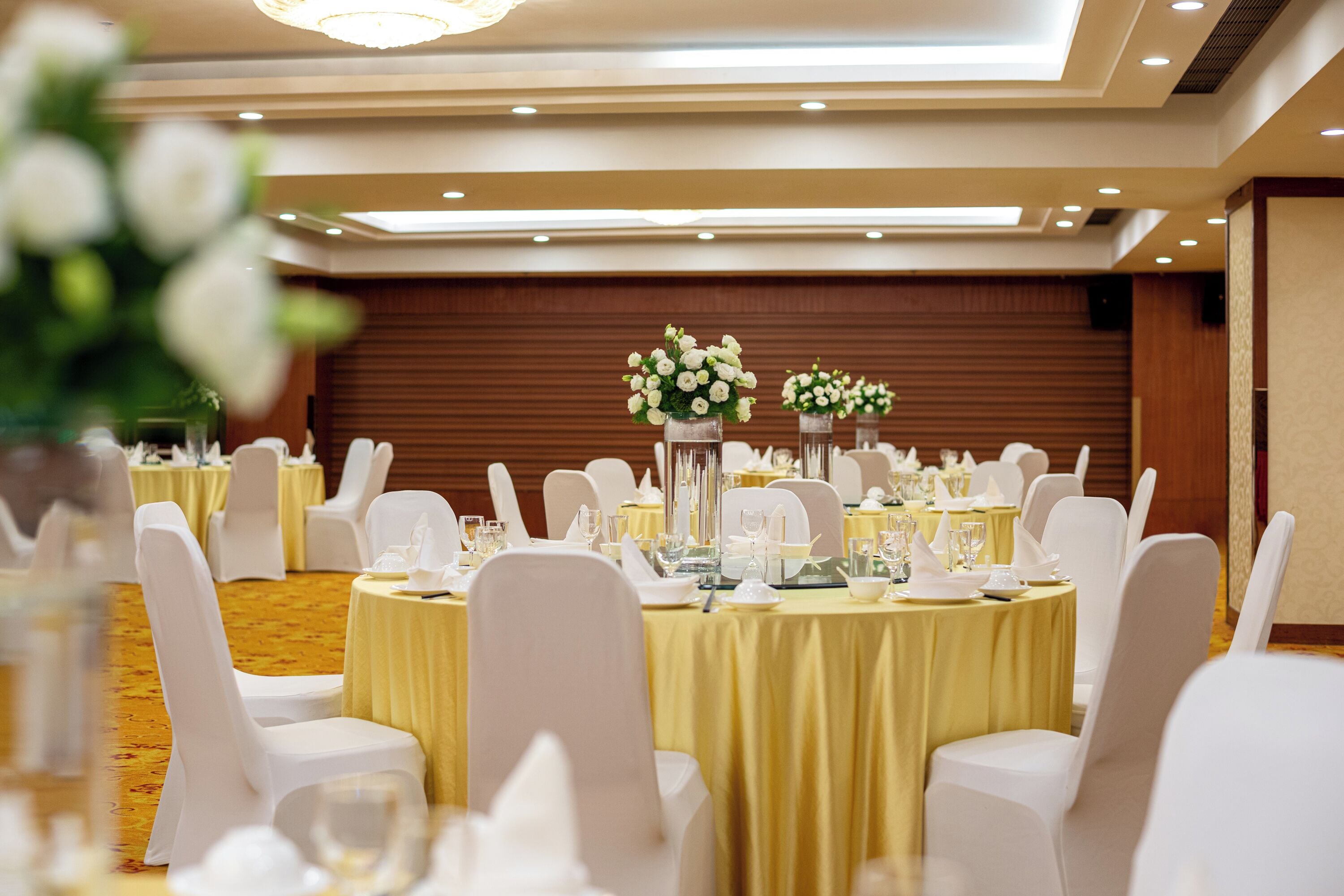 A banquet hall with round tables covered in yellow tablecloths, white chairs, and floral centerpieces.