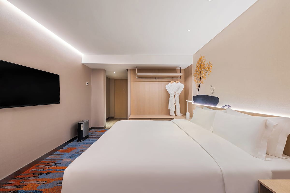 Une chambre d’hôtel moderne dotée d’un grand lit, d’un téléviseur à écran plat fixé au mur, d’une table de chevet et d’un dressing.