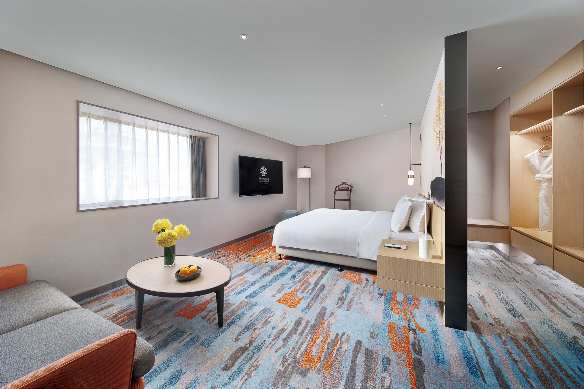 A hotel room with a bed, a seating area with a table, a TV, and a wardrobe.