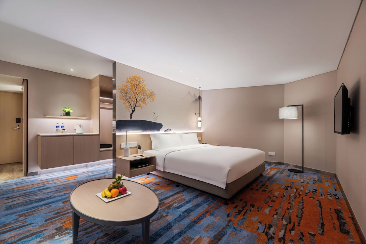 Une chambre d’hôtel moderne équipée d’un lit, d’une table de chevet, d’une lampe et d’un petit coin repas agrémenté d’une assiette de fruits.