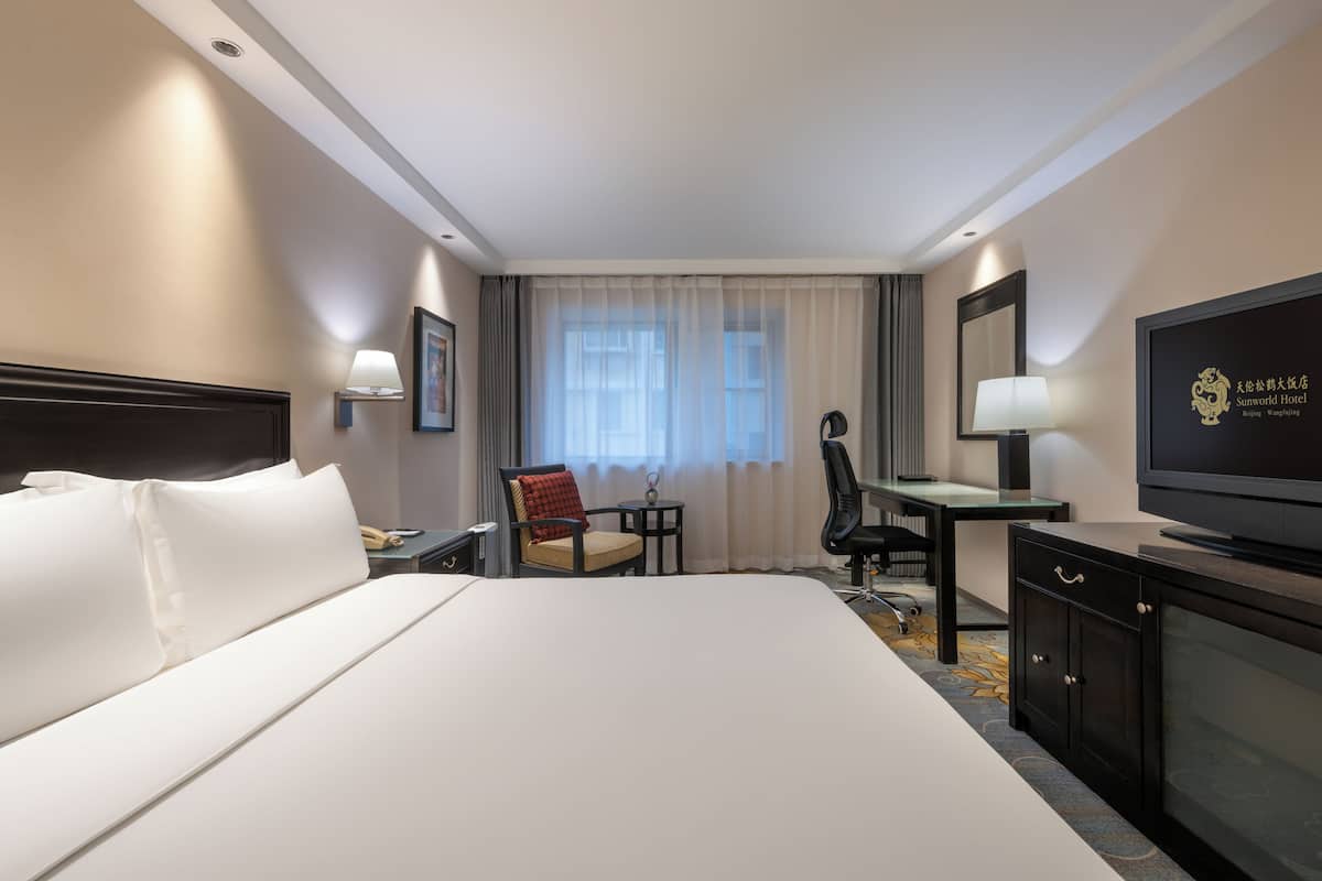 Une chambre d’hôtel avec un grand lit, un bureau, une chaise, une télévision et une fenêtre avec des rideaux.