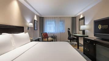 Ein Hotelzimmer mit einem großen Bett, einem Schreibtisch, einem Sessel, einem Fernseher und einem Fenster mit Vorhängen.
