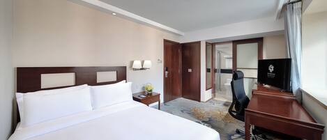 Habitación de hotel con una cama grande, un escritorio con silla, televisor y baño visible a través de una puerta abierta.