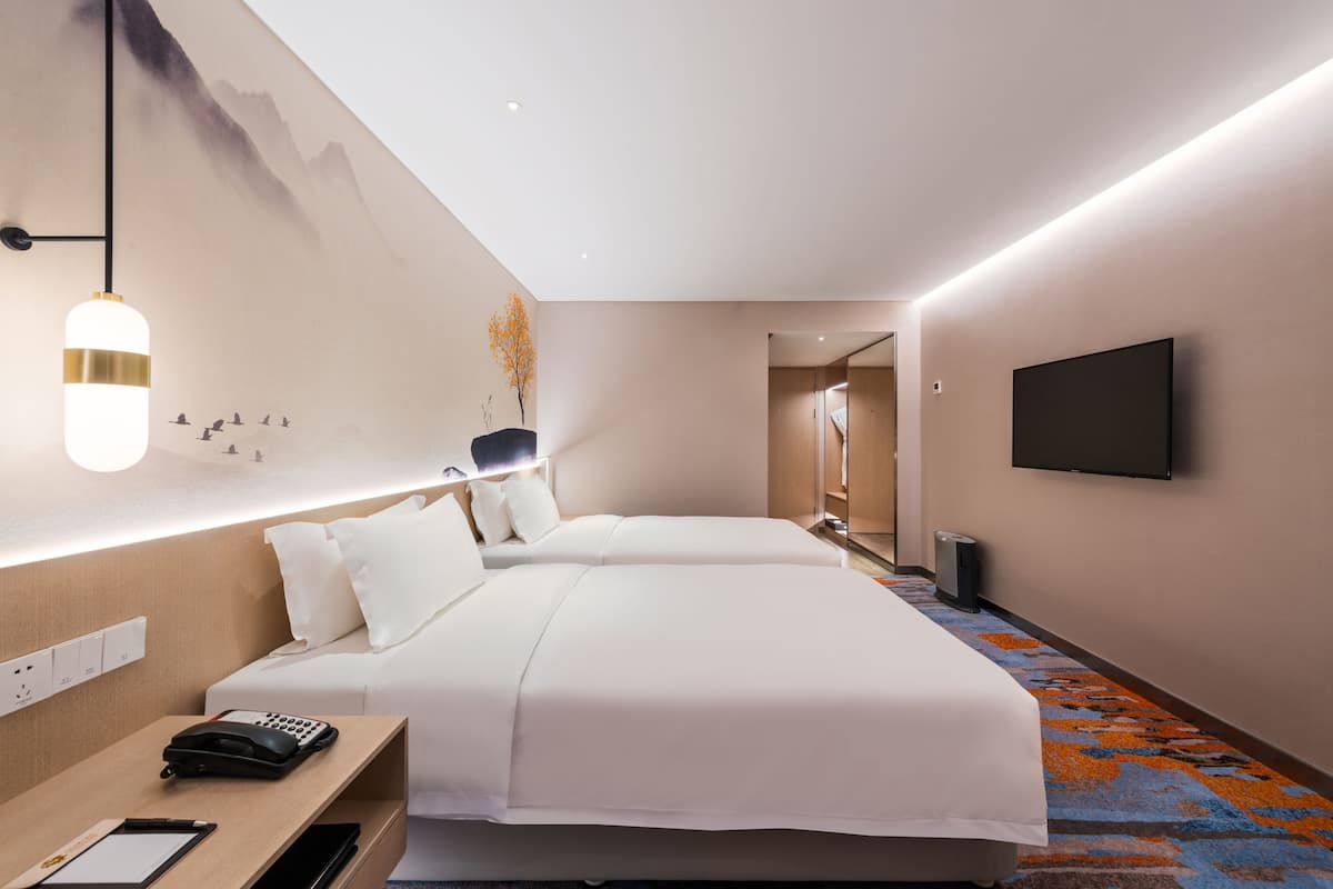 Une chambre d’hôtel avec deux lits, un bureau avec un téléphone, un téléviseur à écran plat et un luminaire fixé au mur.