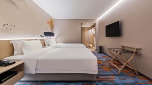 Ein Hotelzimmer mit einem großen Bett, einem flachbildfernseher an der Wand, einem Nachttisch mit Telefon und einem hängenden Handtuchhalter.