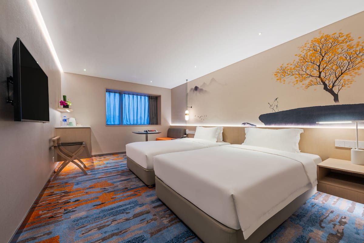 Une chambre d’hôtel avec deux lits, une télévision, un bureau, une chaise, une table de chevet et une fresque murale.