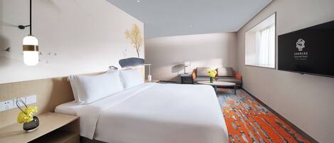 Habitación de hotel con cama, mesita de noche, lámpara y televisor montado en la pared.