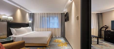 A hotel room with a bed, a desk, a chair, a television, and a carpet with a floral pattern.