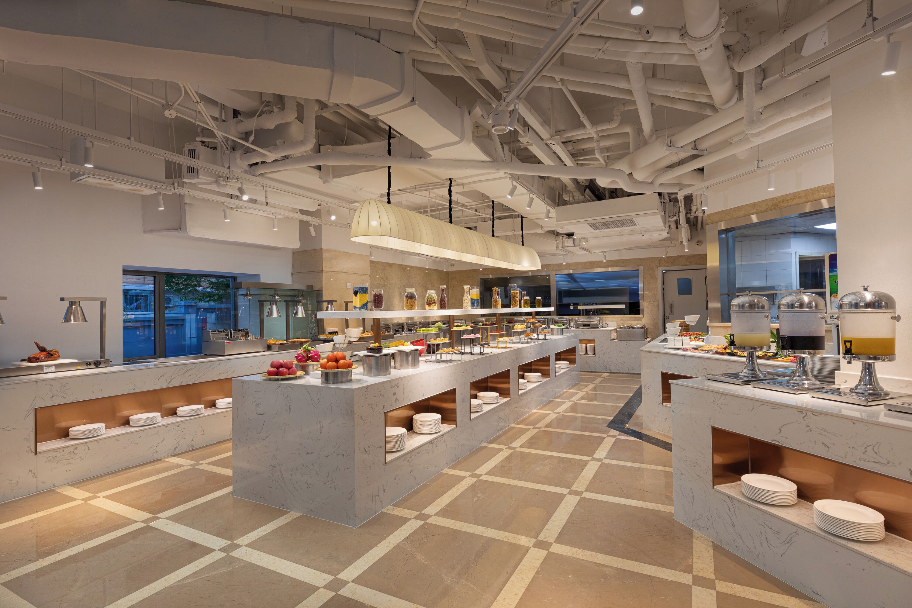 A modern buffet setup with multiple serving stations, a marble floor, and overhead lighting.