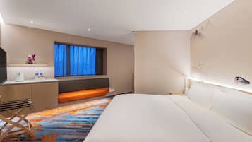A hotel room with a bed, a desk with a chair, a window with curtains, and a wall with a decorative element.