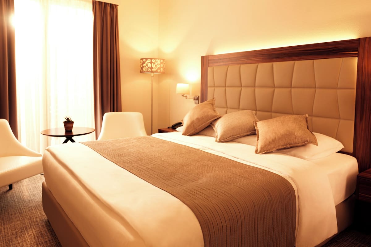 A hotel room with a large bed, a bedside table, a lamp, and a chair.