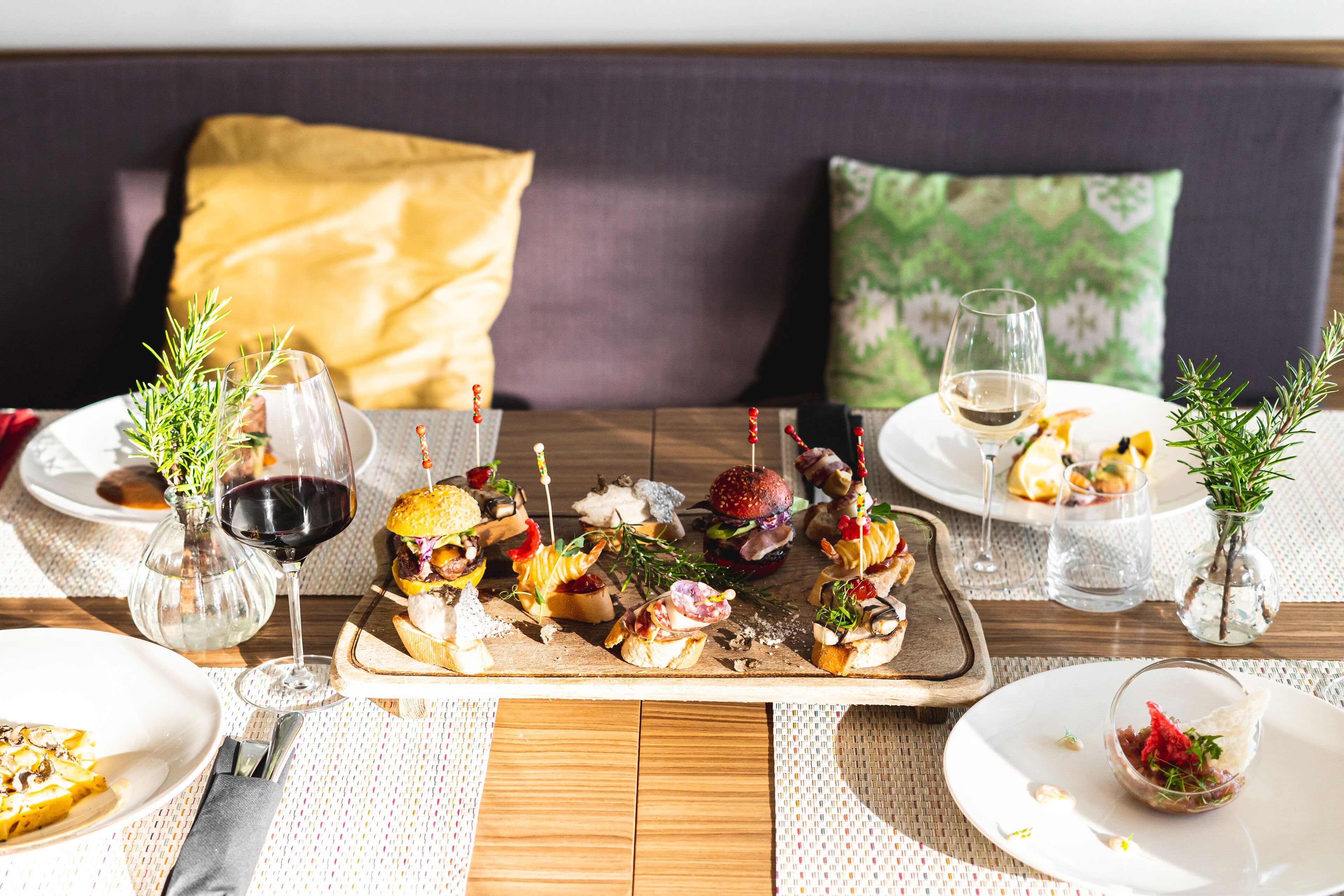 A dining table with various appetizers, wine glasses, and a wooden board with food items.
