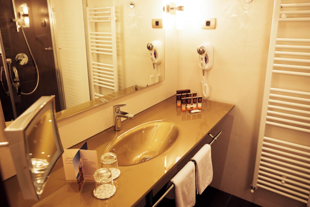 Un baño con un espejo grande, un lavabo, toallero, secador de pelo y ducha.