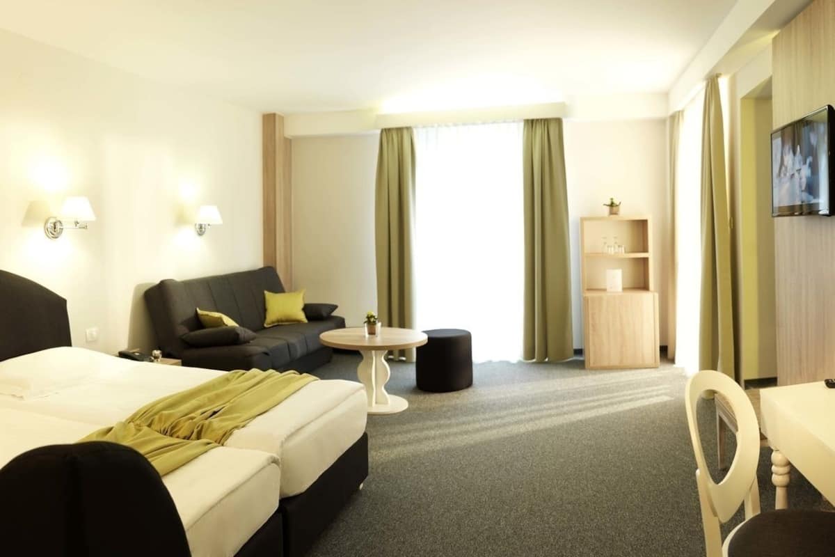 A hotel room with a bed, a sofa, a small round table, a TV, and a cabinet.