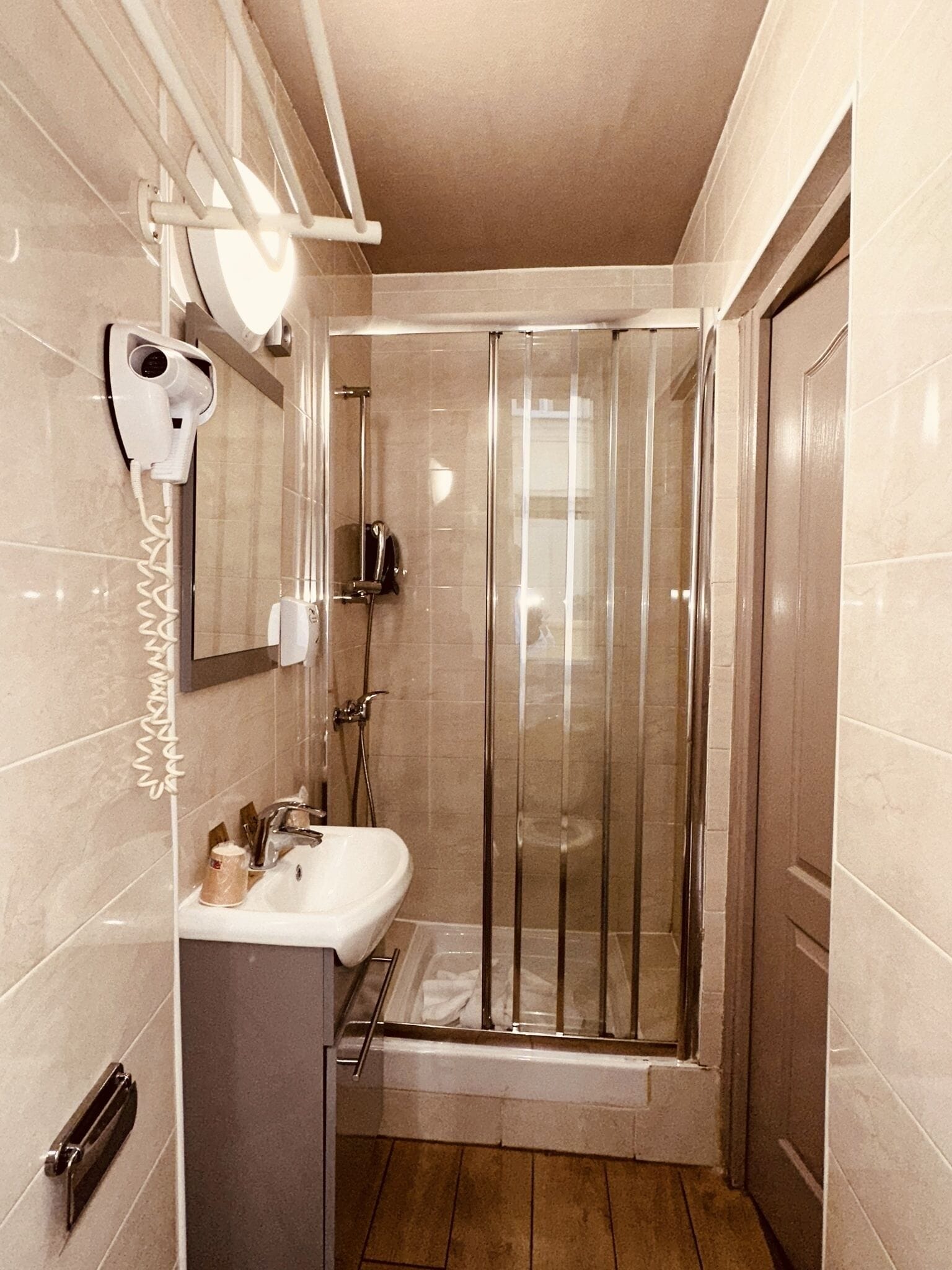 Une salle de bain moderne avec une douche à parois de verre, un lavabo blanc et un sèche-cheveux fixé au mur.