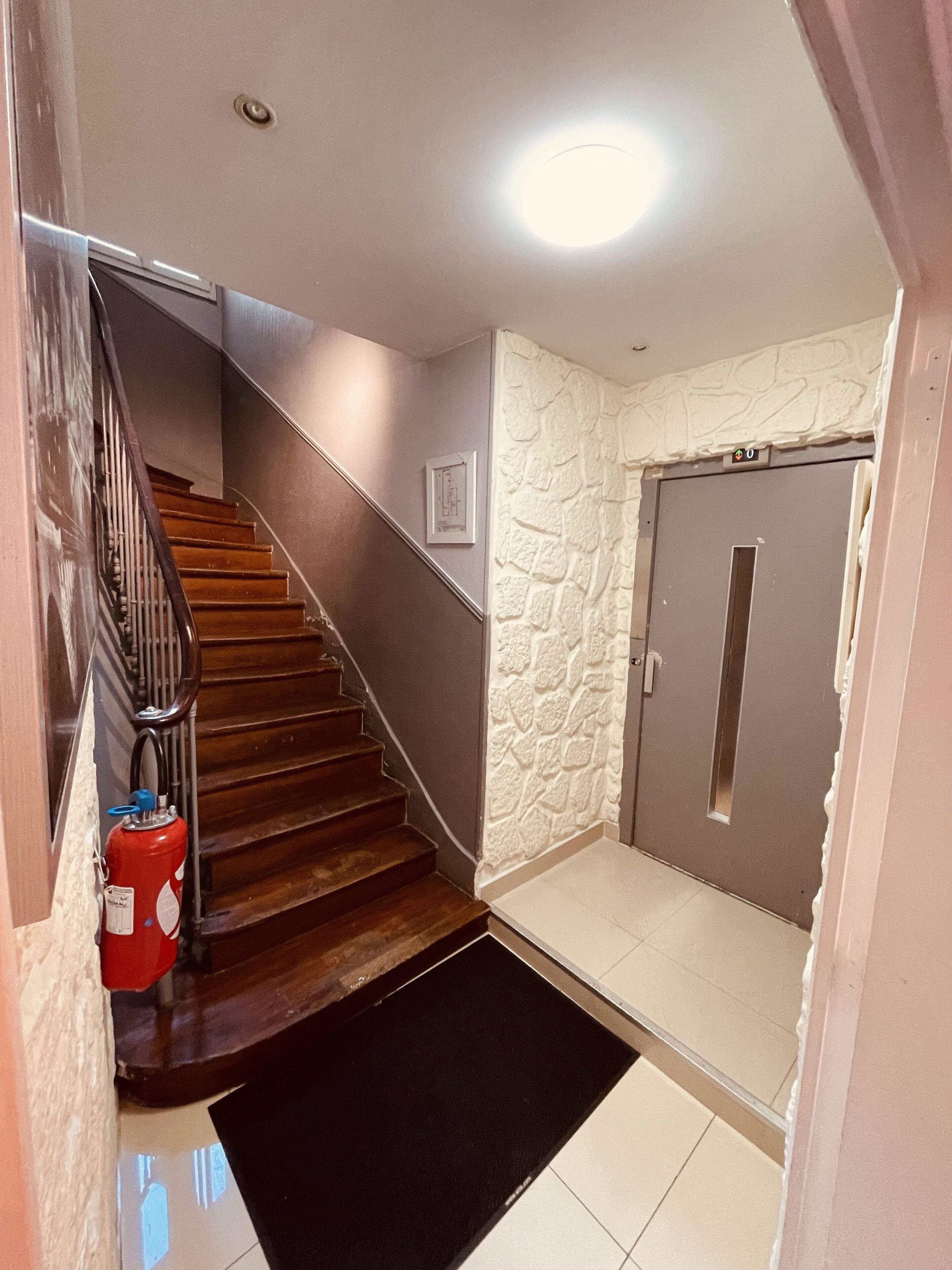 A staircase with wooden steps and a metal railing, leading to a door with a stone-textured wall.