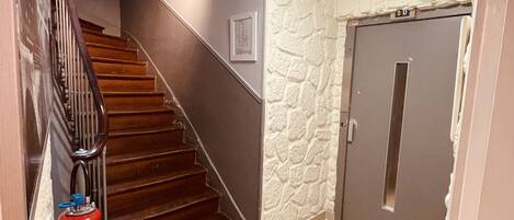 A staircase with wooden steps and a metal railing, leading to a door with a stone-textured wall.